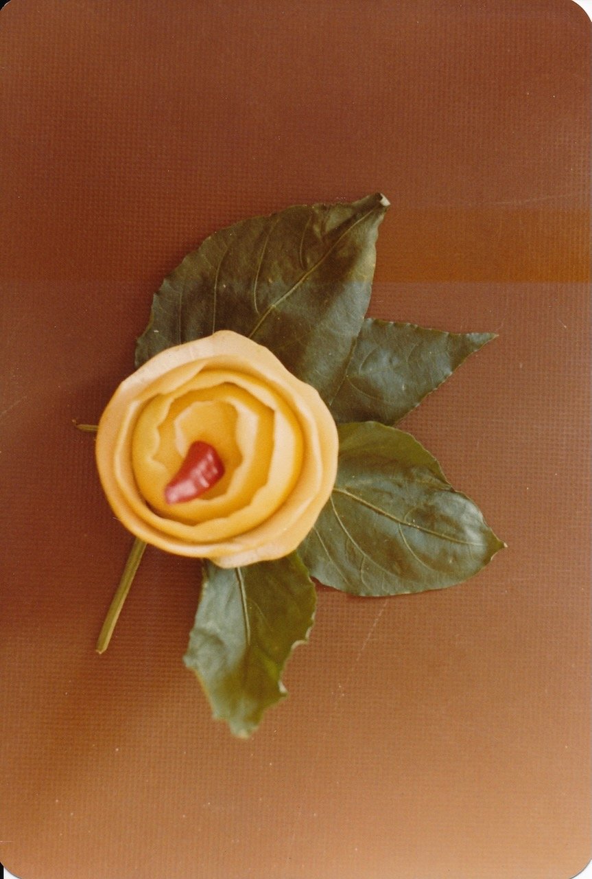 Yellow rose-shaped vegetable garnish with green leaves on brown background.